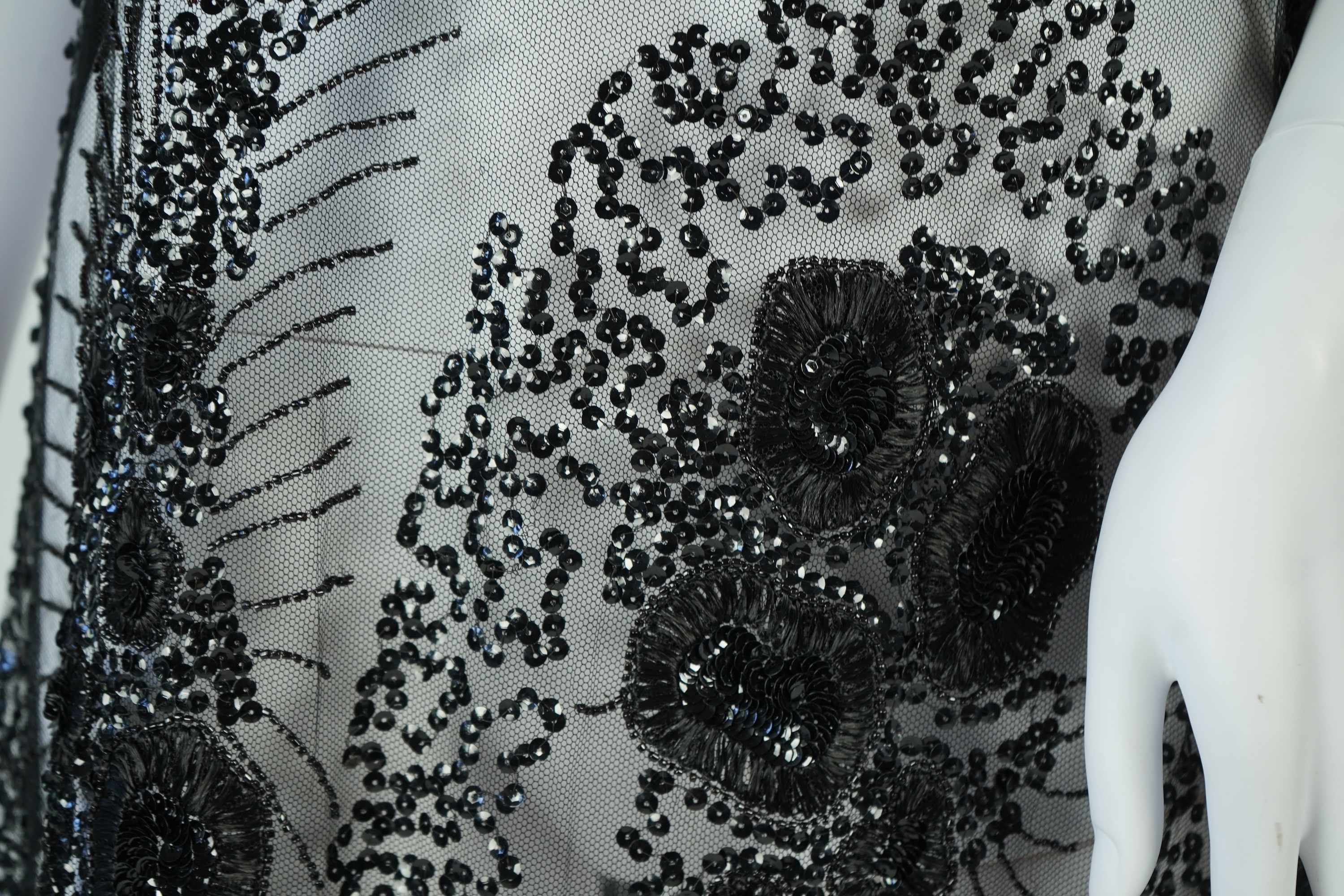 A 1920's black sequin on net tabard, with floral decoration and two side sequinned straps. Length 97cm. Condition - a few sequins have detached but are in a bag for re-attaching.